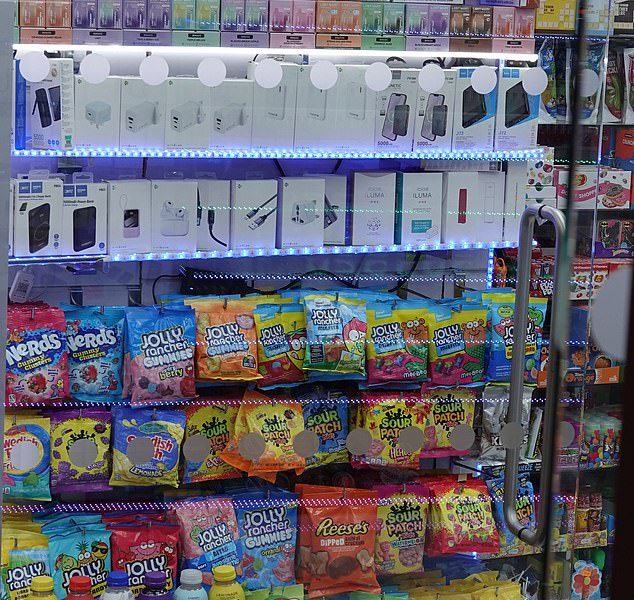 A row of 'snus' nicotine pouches and vapes are sold above bags of sweets and popular Prime drinks on Oxford Street