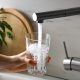 A woman's hand holds a glass below a faucet as it fills with drinking water